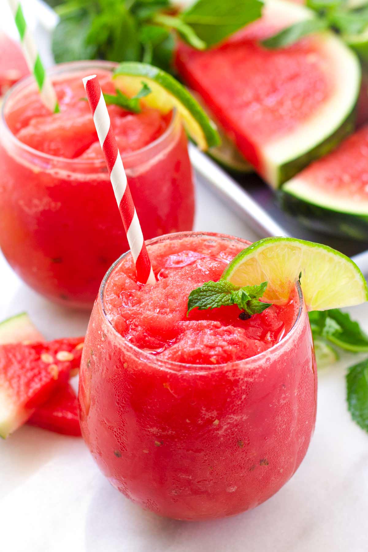 two glasses of watermelon slushies with lime garnish