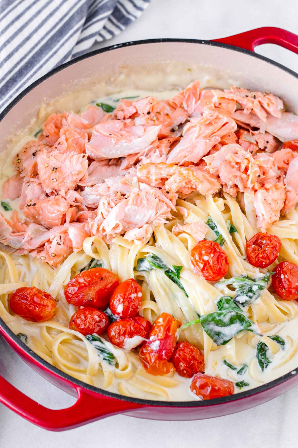 pieces of roasted salmon sitting on top of a bed of pasta and tomatoes