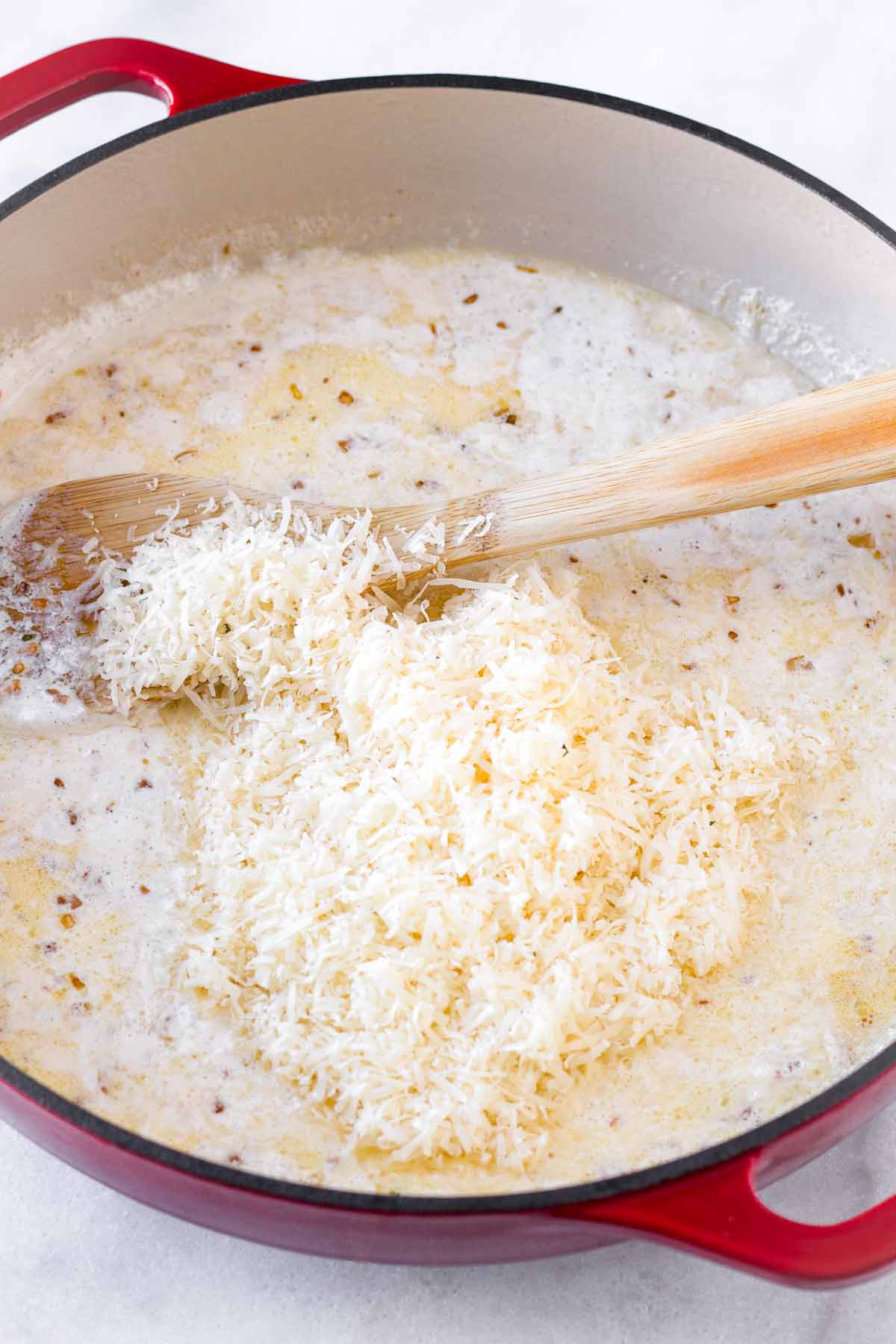 grated parmesan cheese on top of creamy sauce in a pot
