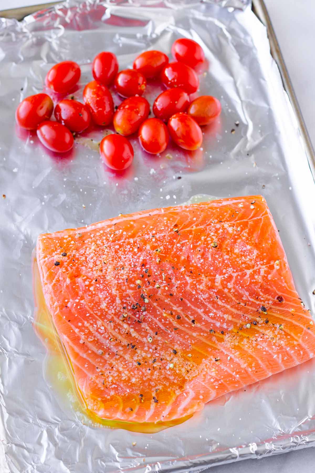 an unbaked salmon filet and cherry tomatoes on sheet pan