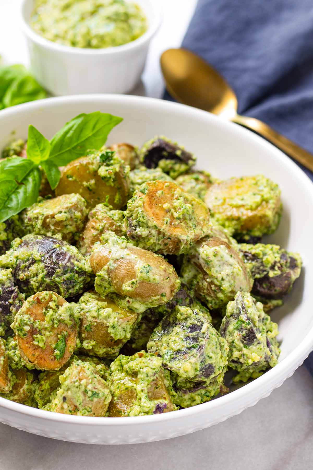bowl with creamy pesto potato salad with napkin and spoon in the back