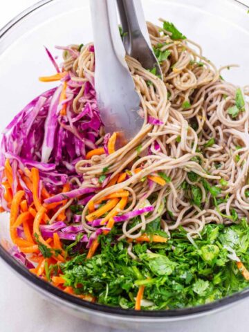 tossing noodles with slices vegetables in a bowl using tongs