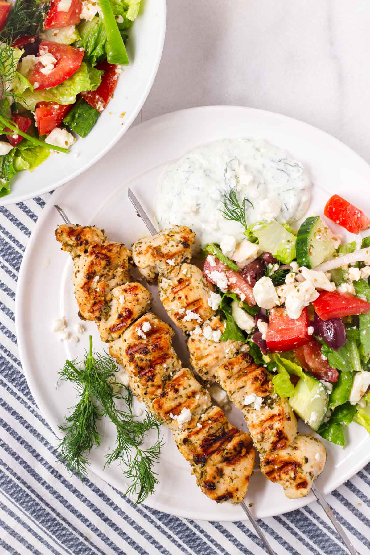 two chicken kabobs on plate with side of salad and tzatziki