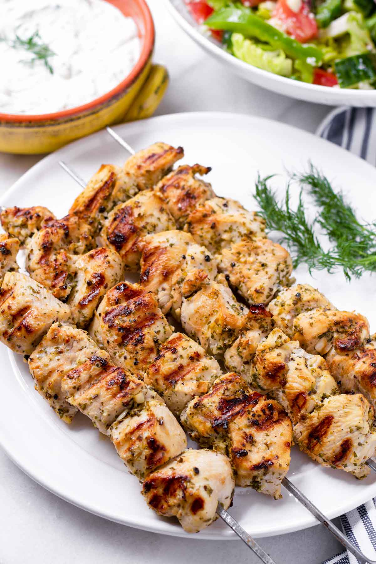 grilled chicken skewers with sauce and salad on the side