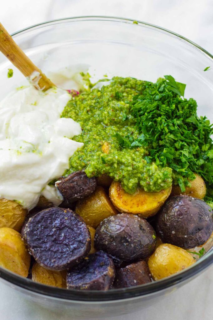 glass bowl with potatoes, yogurt, pesto, and parsley