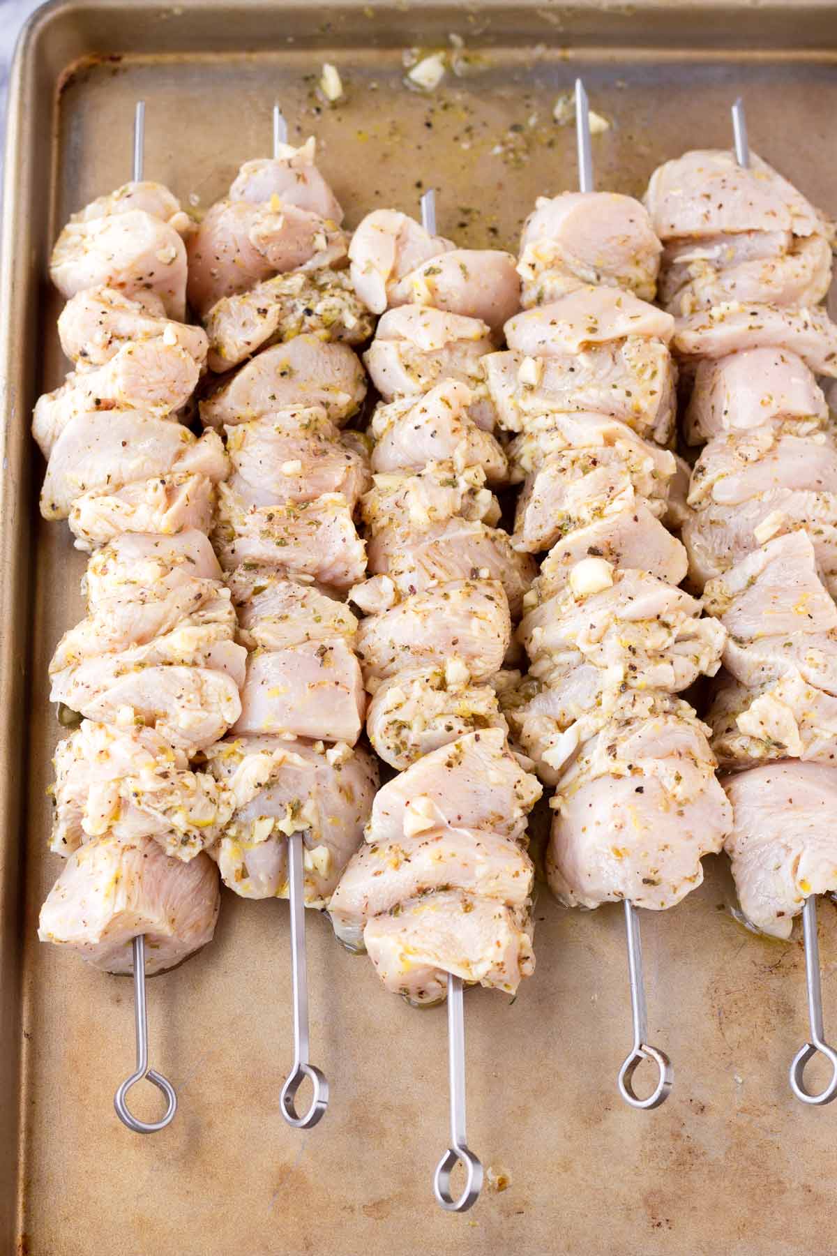 skewered chicken uncooked on a sheet pan