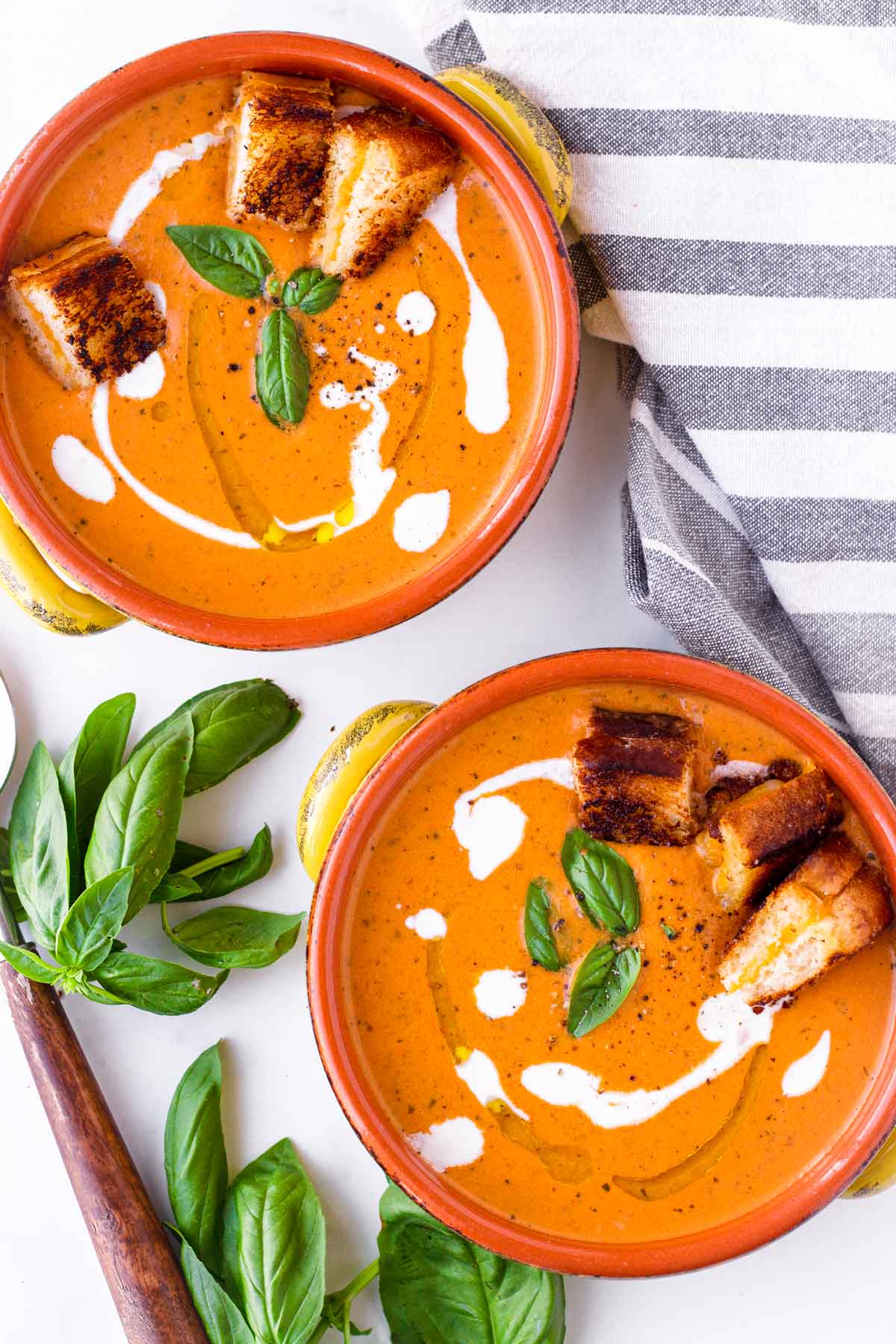 two bowls of tomato basil bisque with garnish