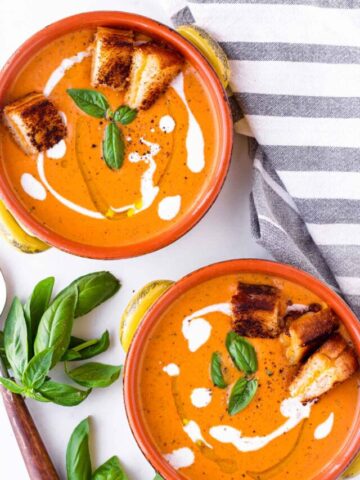two bowls of tomato basil bisque with garnish