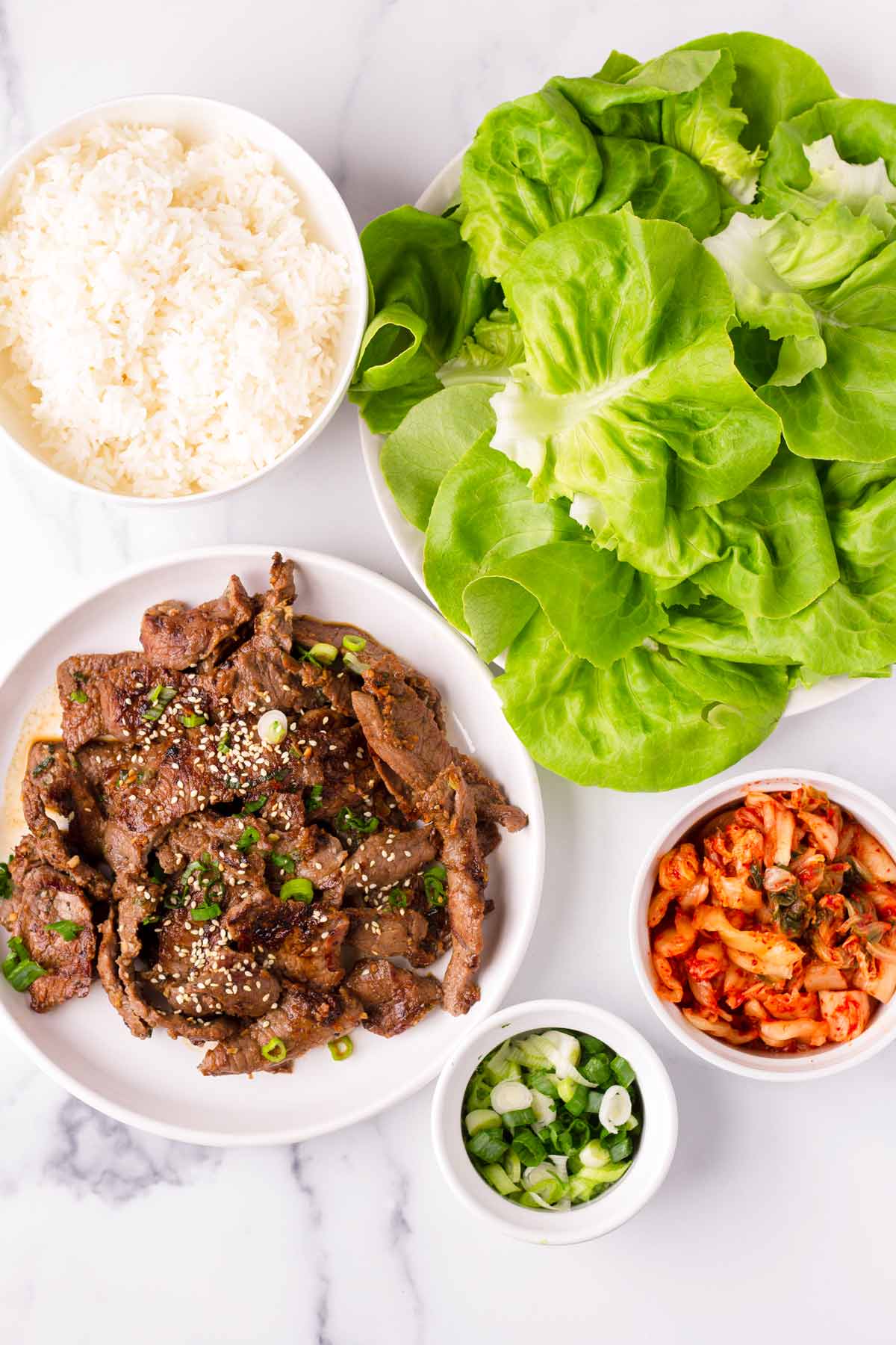 a spread of cooked beef, kimchi, scallions, rice, lettuce