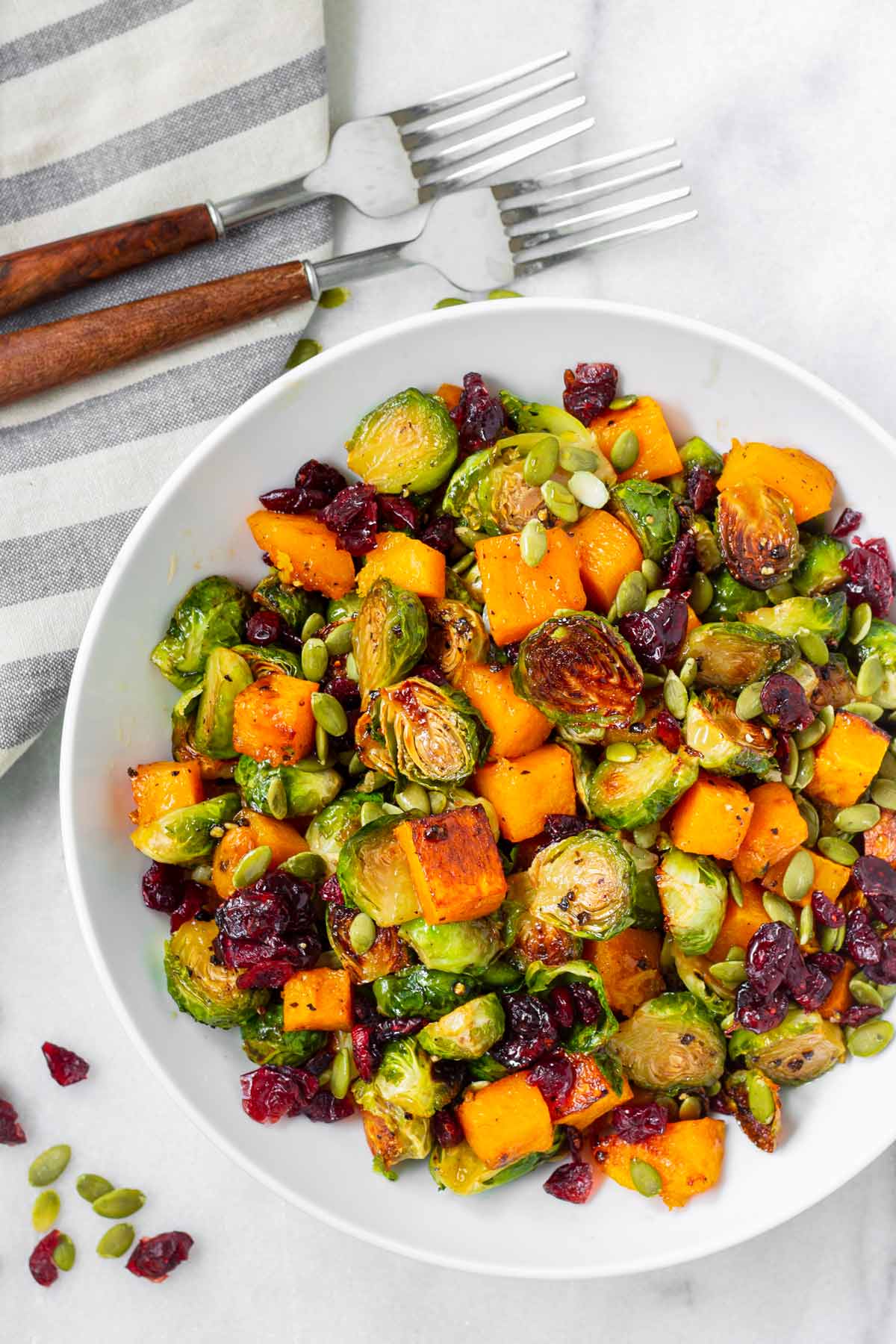 bowl of roasted squash and brussel sprouts next to forks and napkin