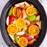 cut up apples, oranges, cinnamon sticks, and cloves in slow cooker