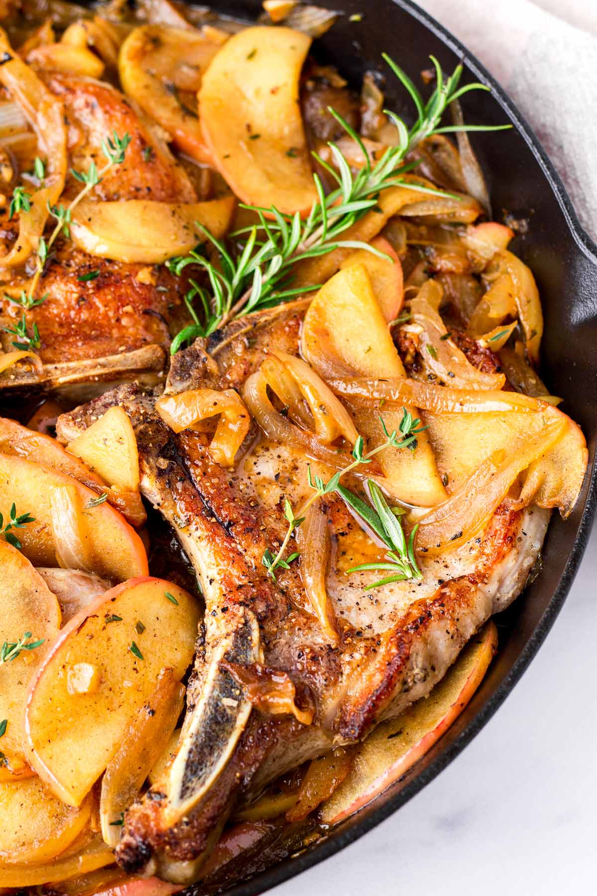close up of skillet bone in pork chops with apples and rosemary garnish