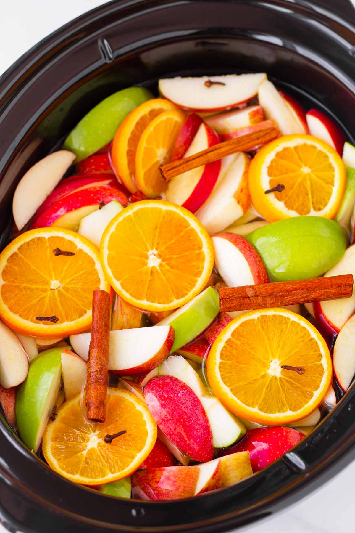fresh apples and oranges in the pot of a slow cooker