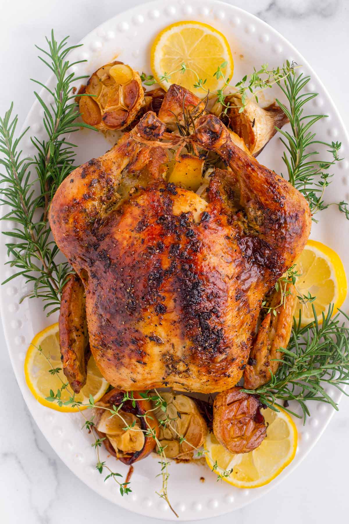 a golden brown whole roasted chicken on a decorated platter
