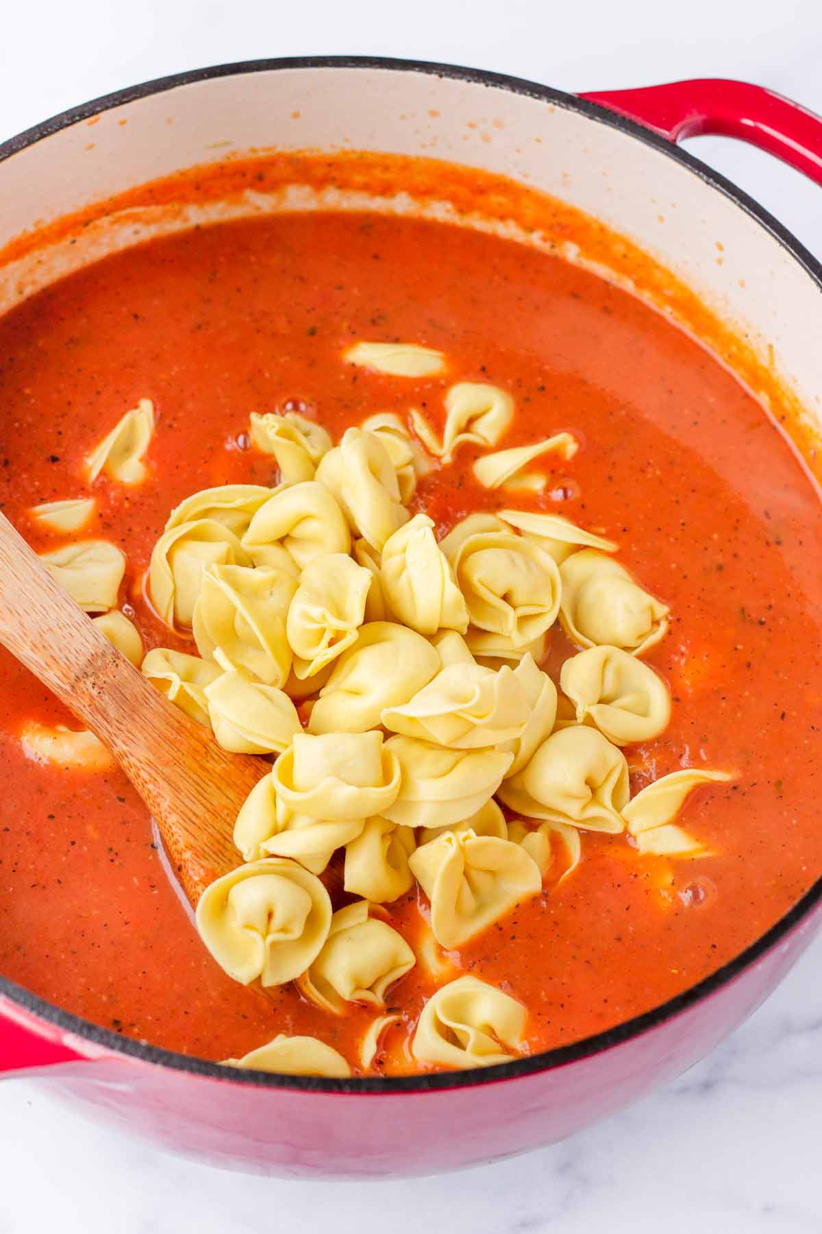 adding cheese tortellini to the tomato broth in the pot