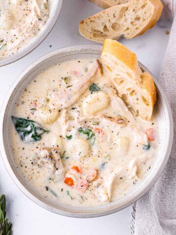 a bowl of creamy gnocchi soup with chicken and bread on the side