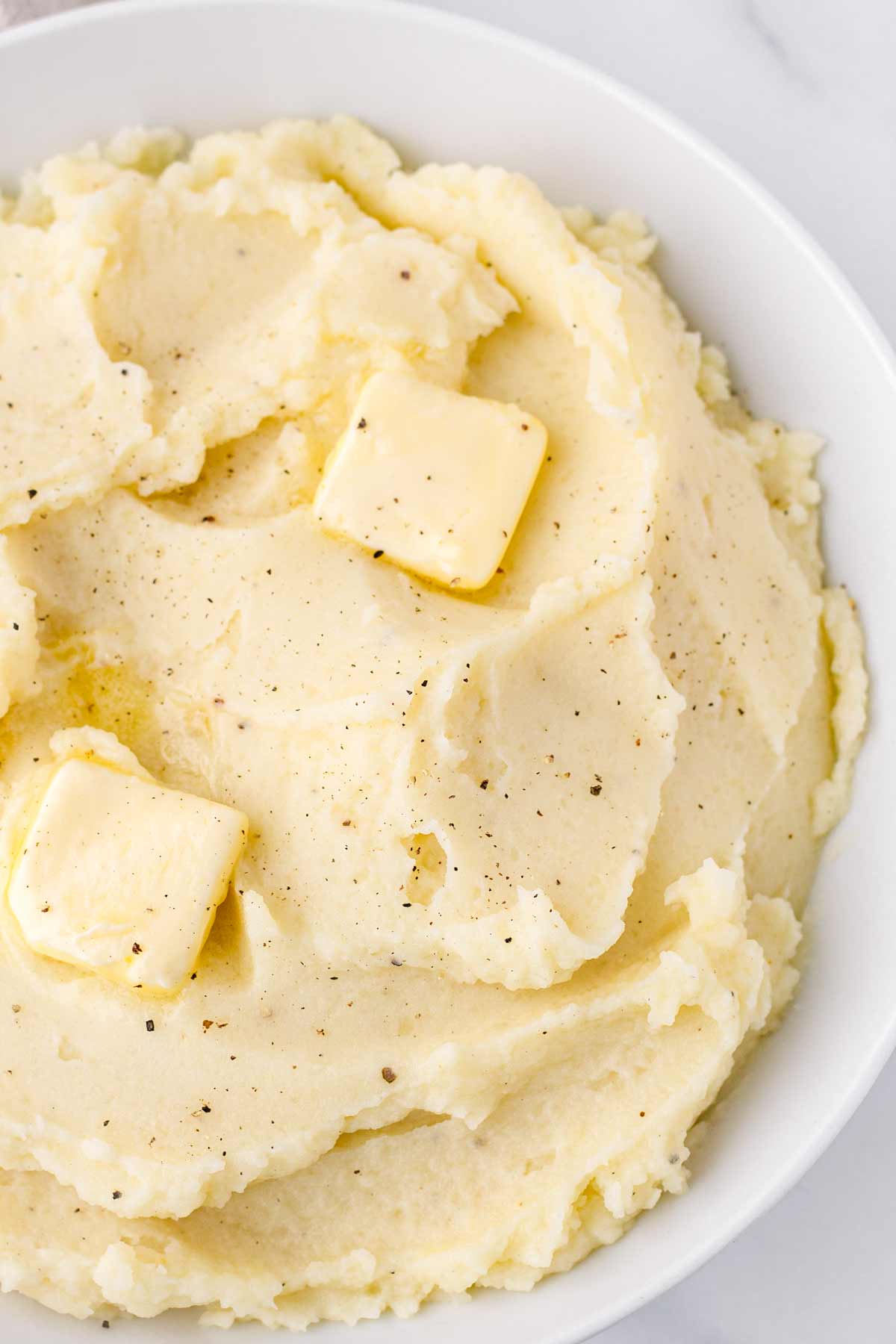 close up of fluffy mashed potatoes with butter and pepper