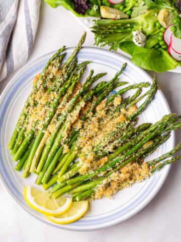 a plate with baked parmesan asparagus next to a salad platter