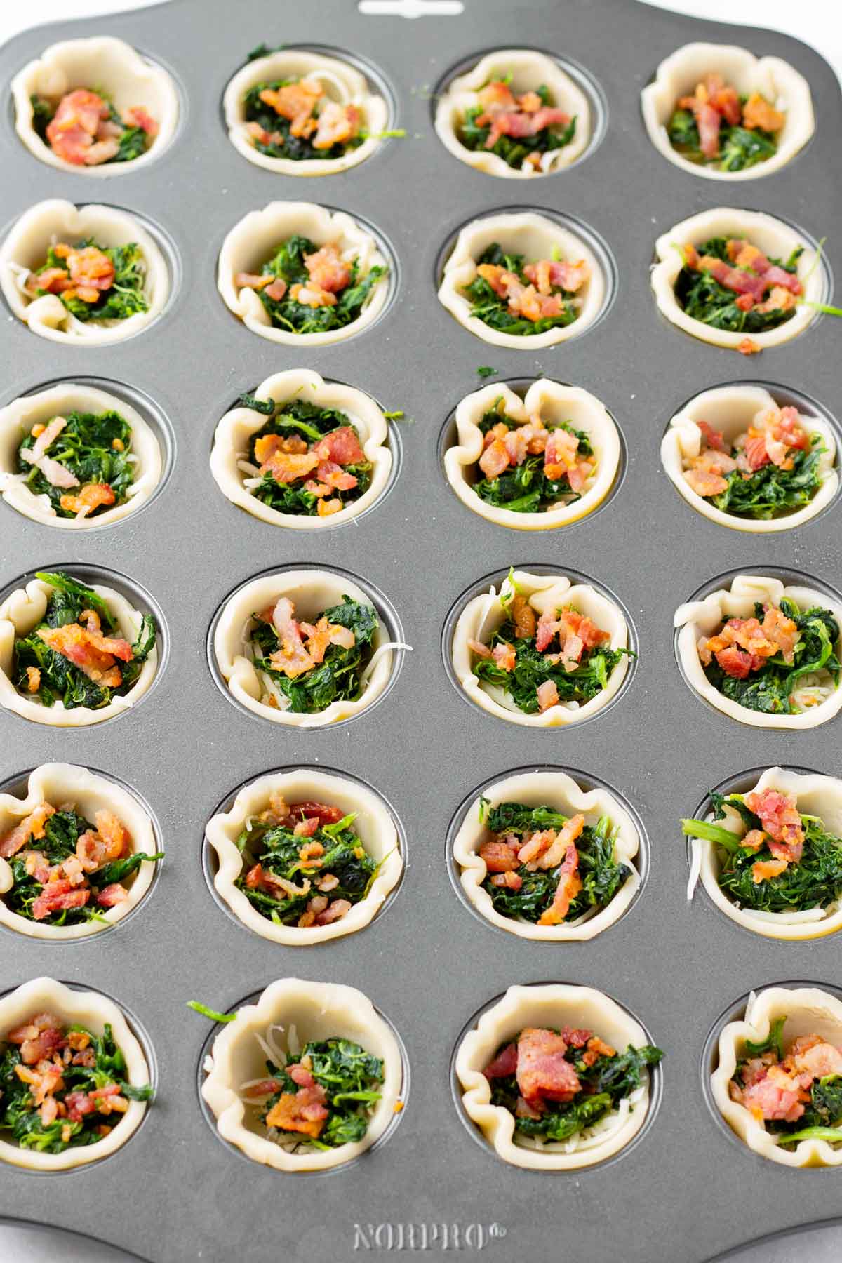 adding spinach and bacon to the pie crust cups