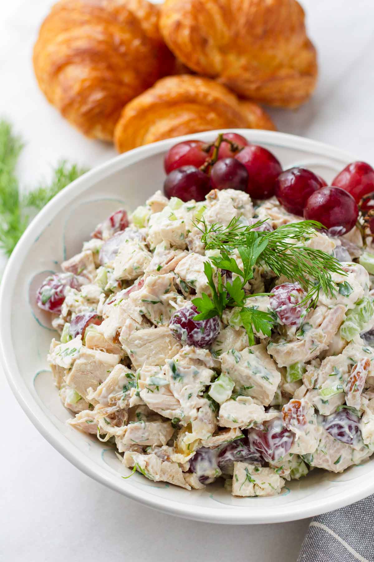 a bowl of creamy chicken salad with grapes and a side of croissants