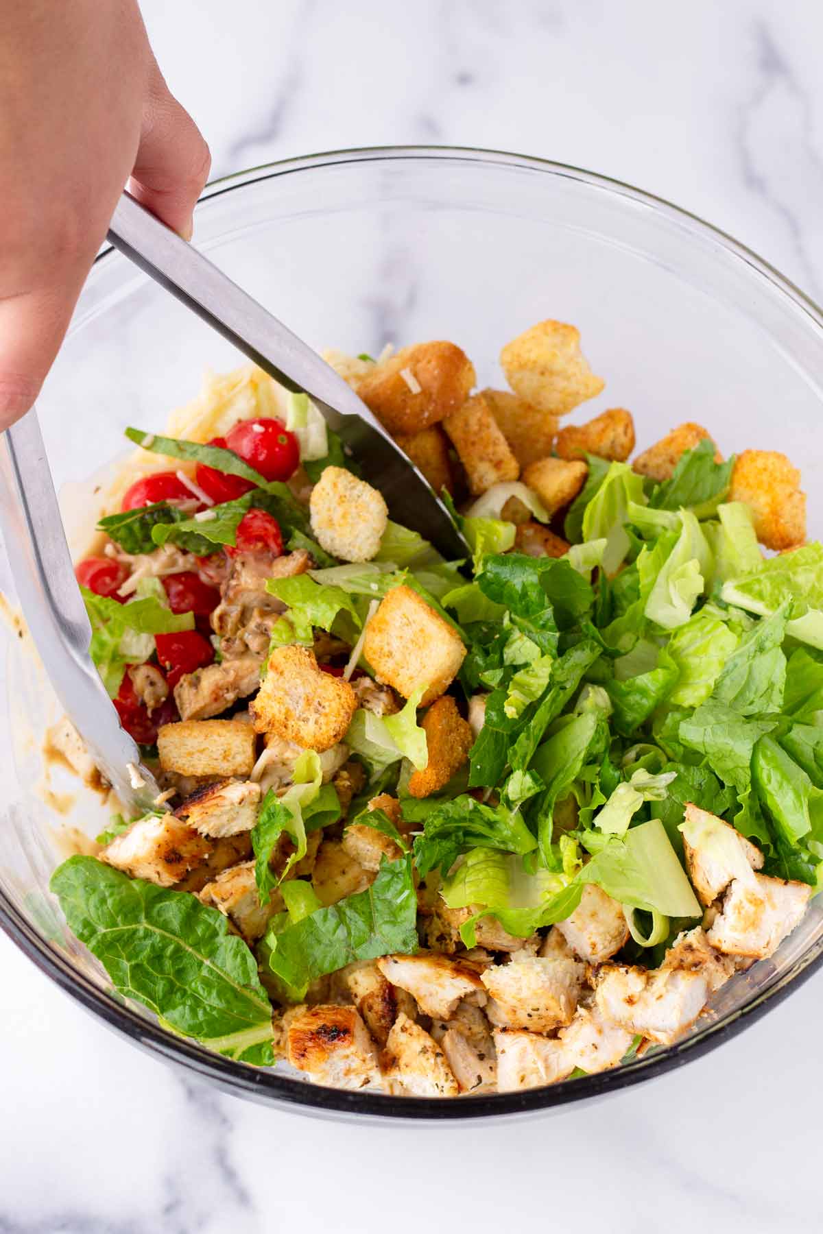 tossing salad ingredients in a bowl using tongs