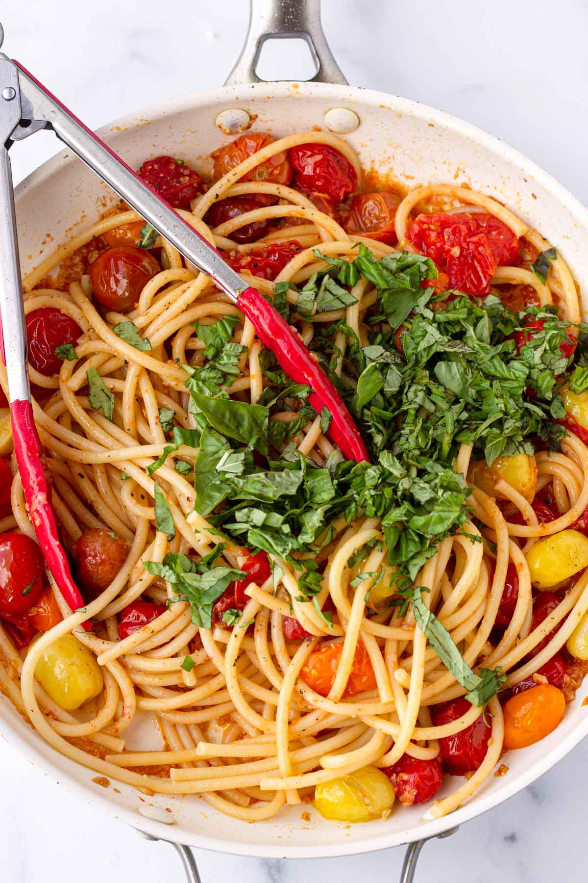 tossing basil with the cooked bucatini and tomatoes