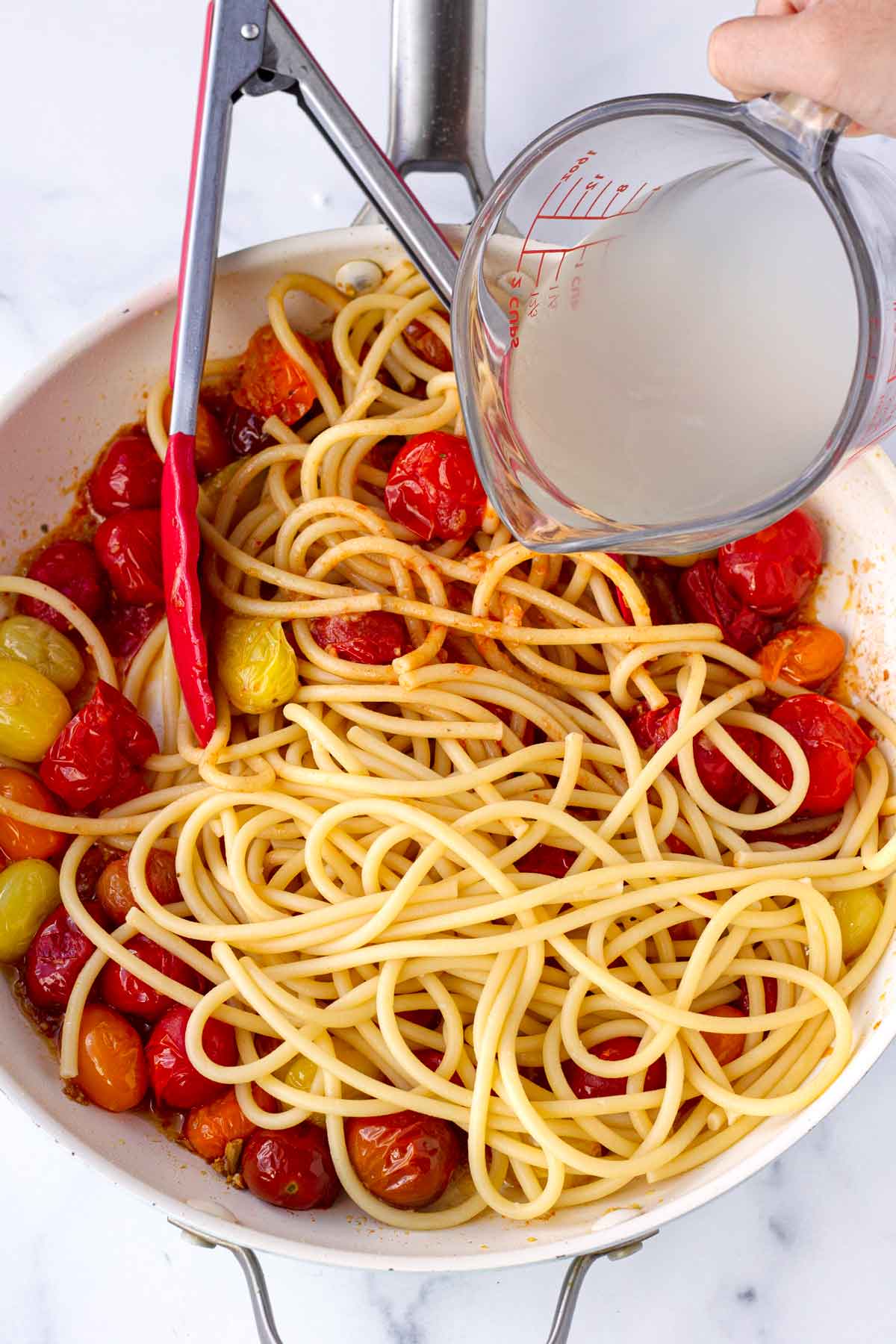 adding reserved pasta water to the pasta in skillet