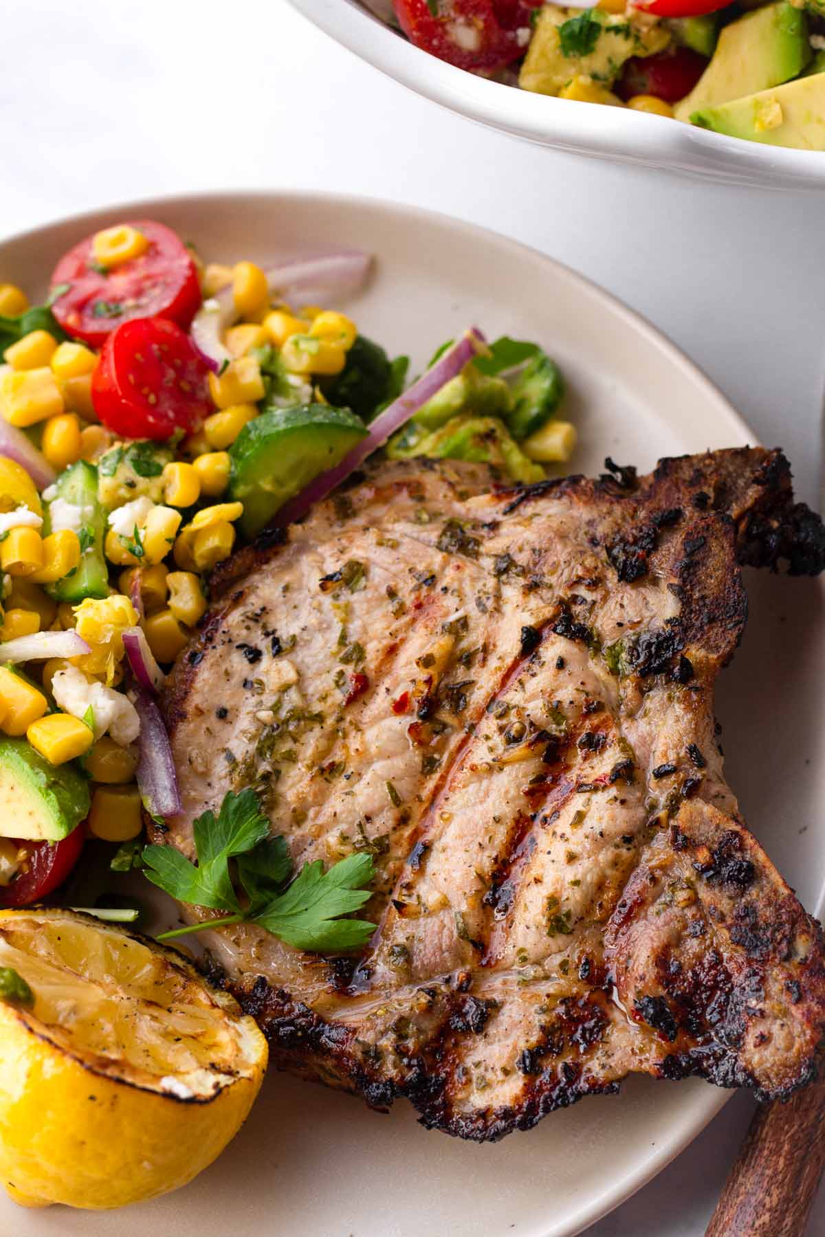 a grilled pork chop with a side of grilled lemon and corn salad