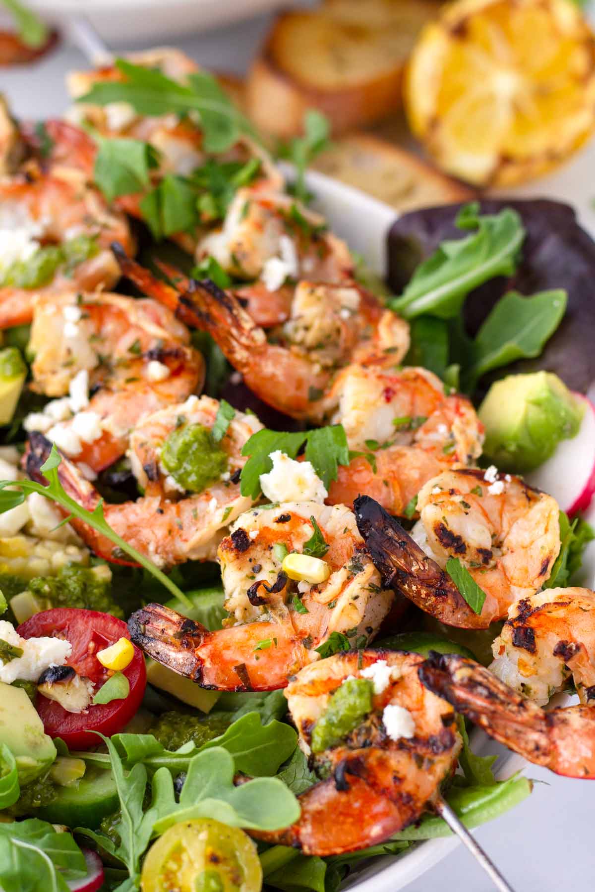 two skewers of grilled shrimp on top of green salad