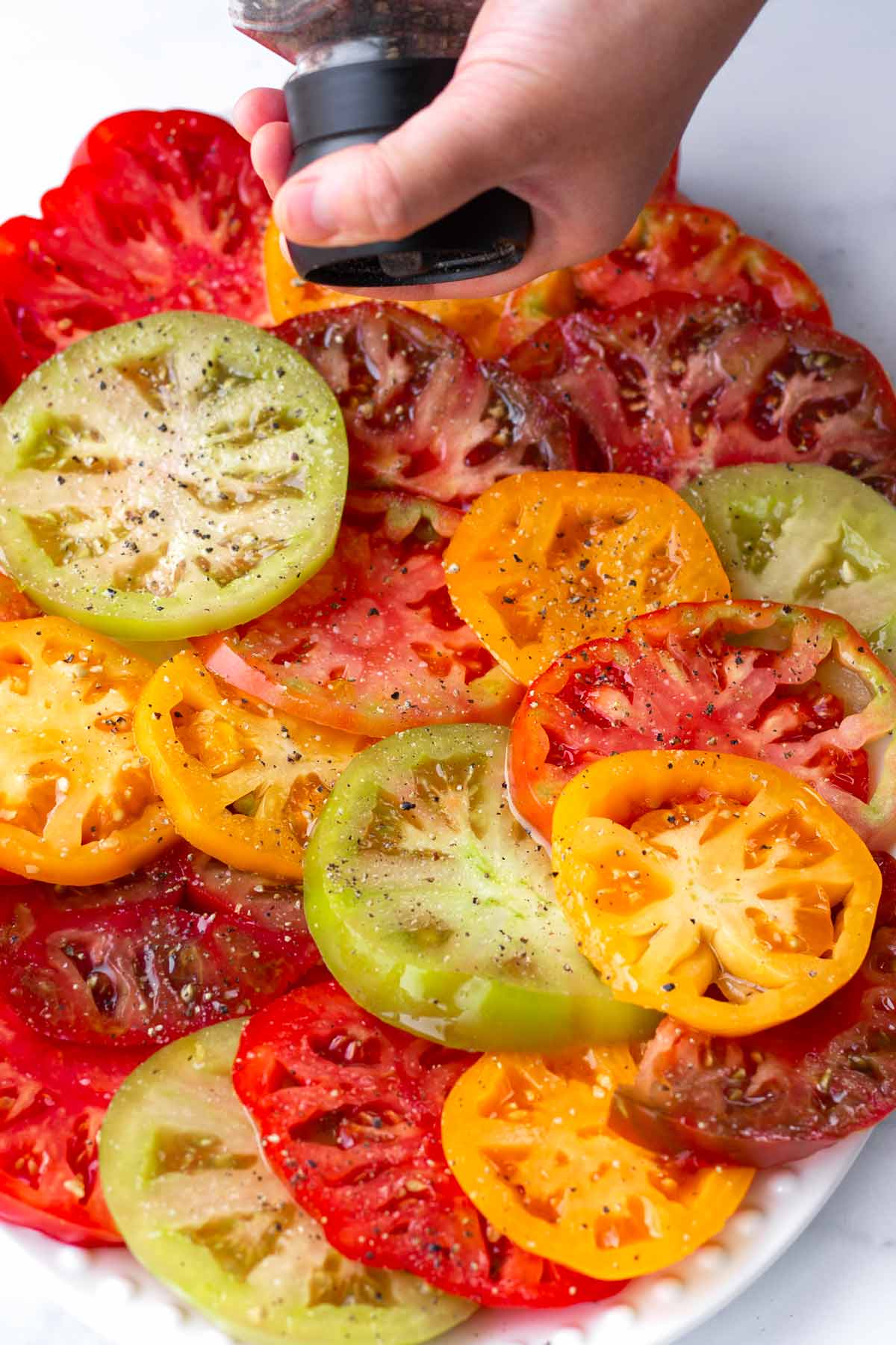 adding pepper onto sliced heirloom tomatoes