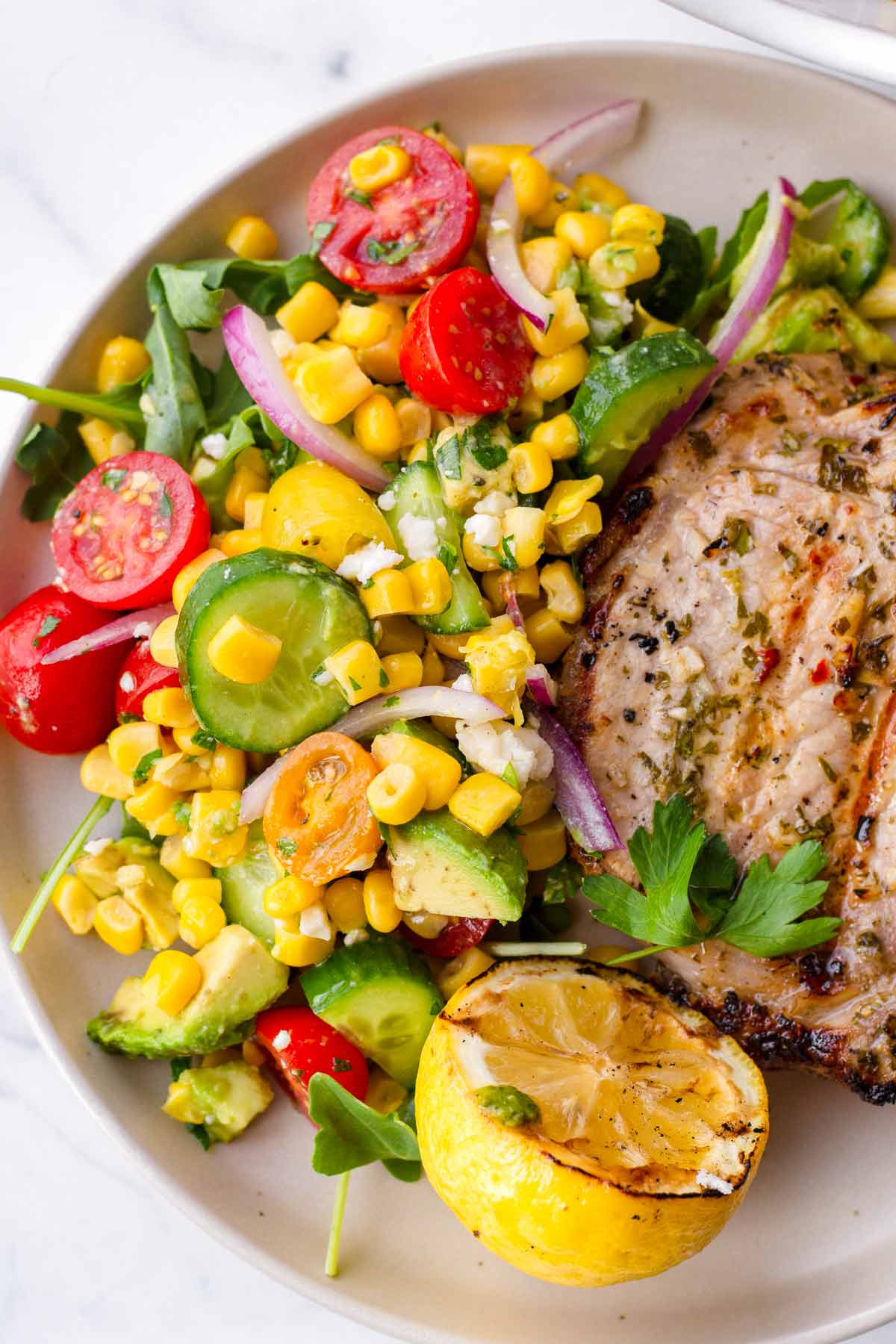 a side of corn salad with pork chop and grilled lemon
