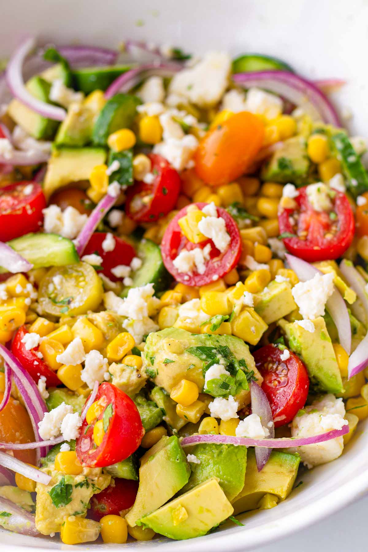 bowl of avocado corn salad with tomatoes and feta