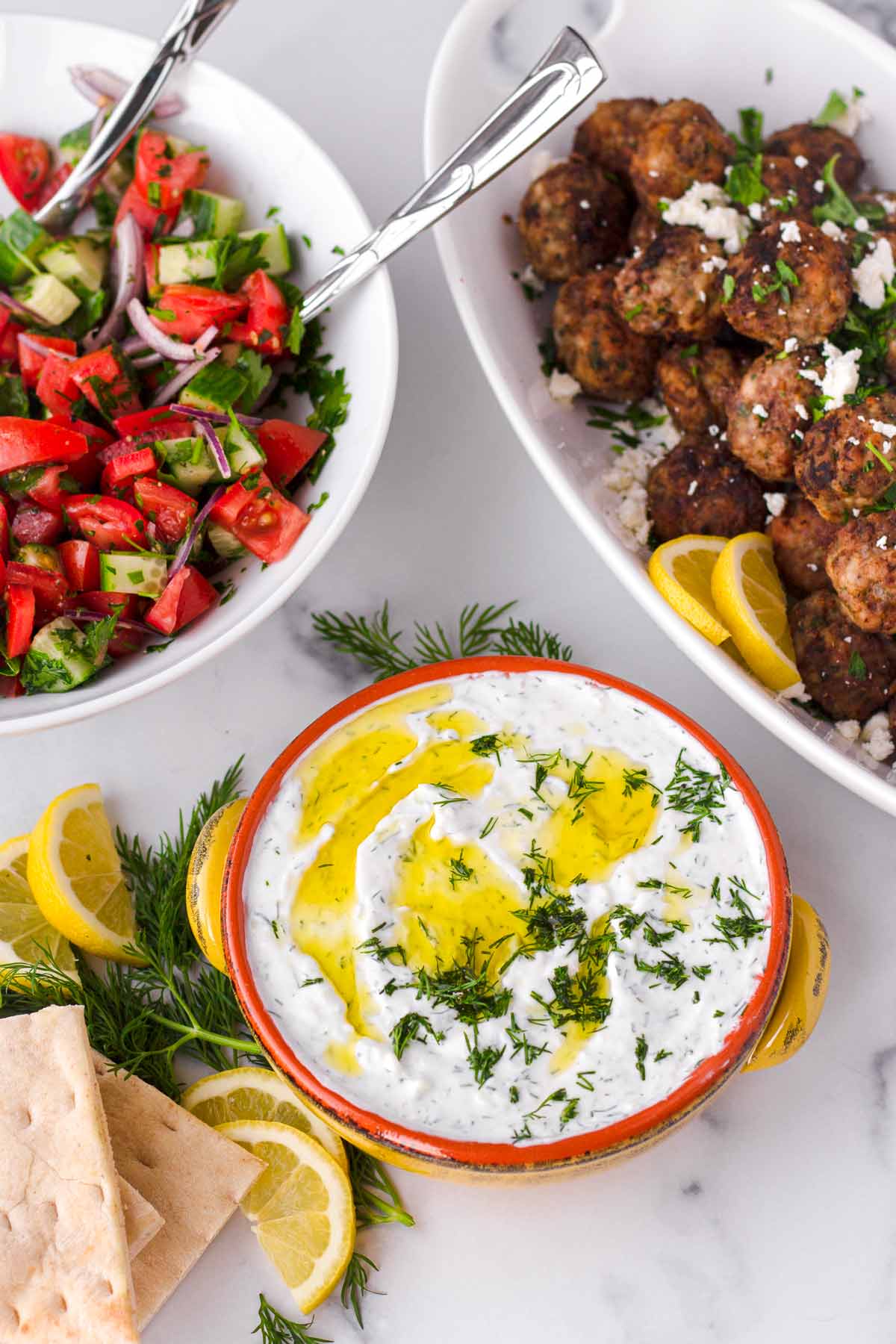 a spread of greek yogurt dip, tomato salad, and greek meatballs