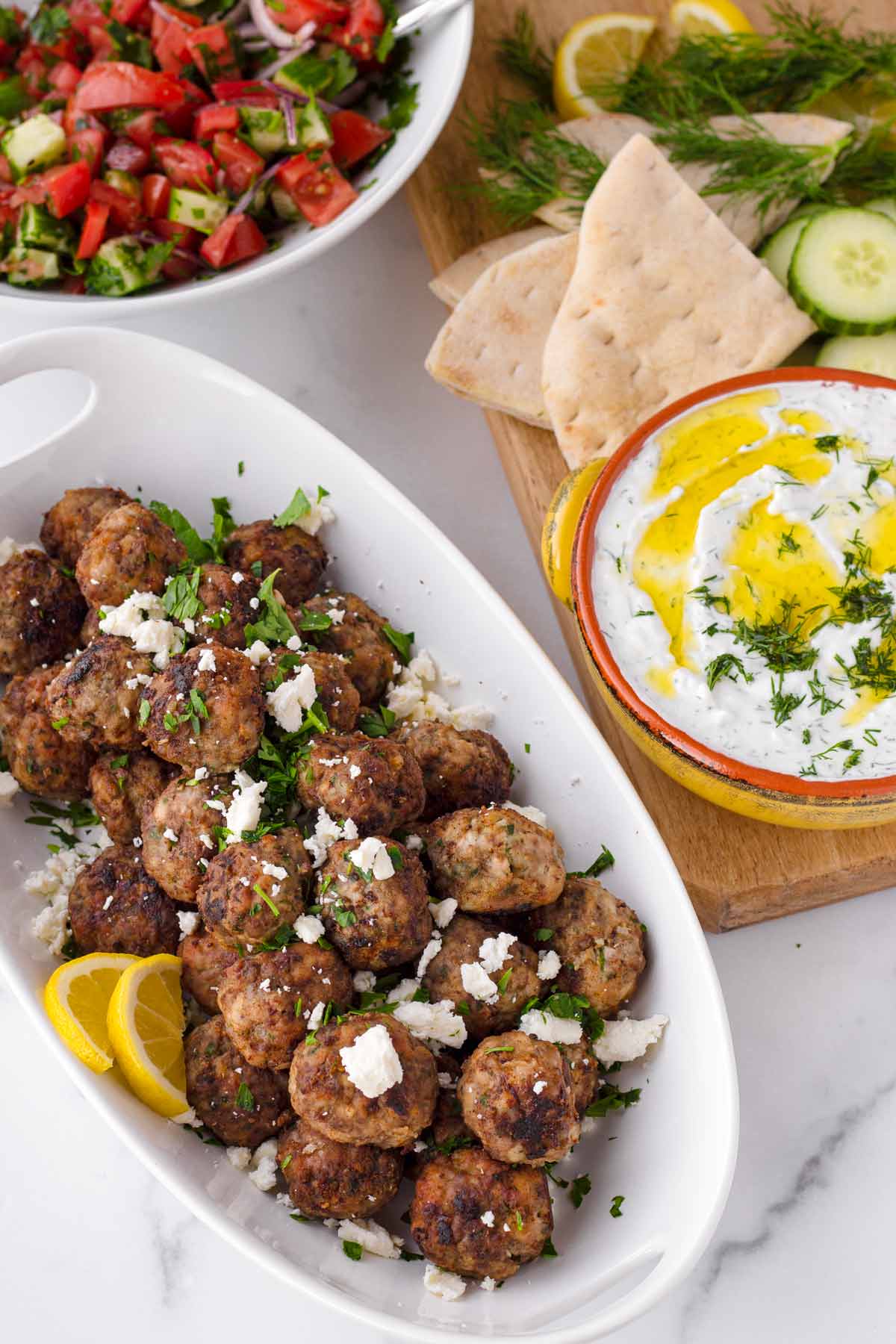 keftedes with a spread of tzatziki, cucumber salad, and bread