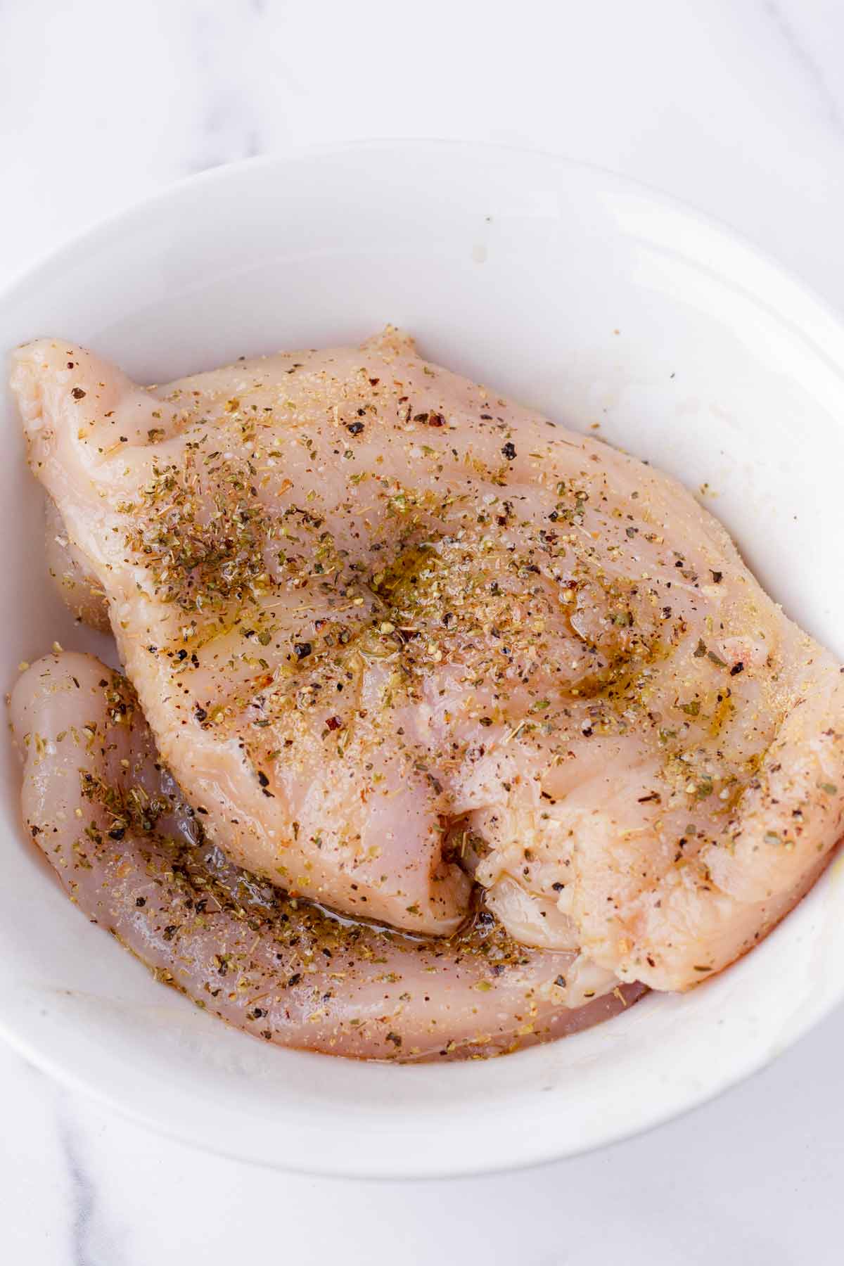 seasoned raw chicken breasts with seasoning in bowl