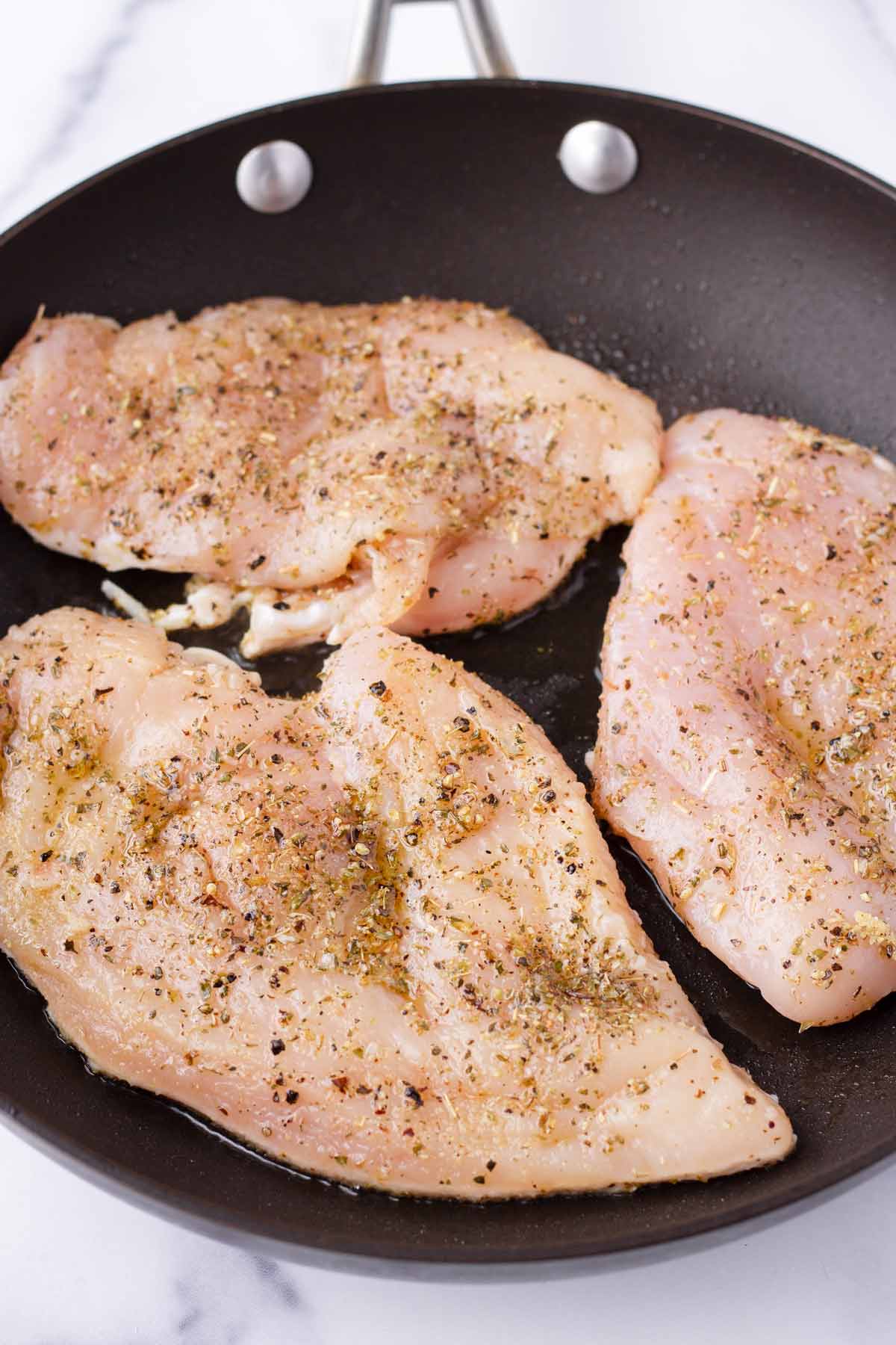 cooking three chicken breasts in a skillet