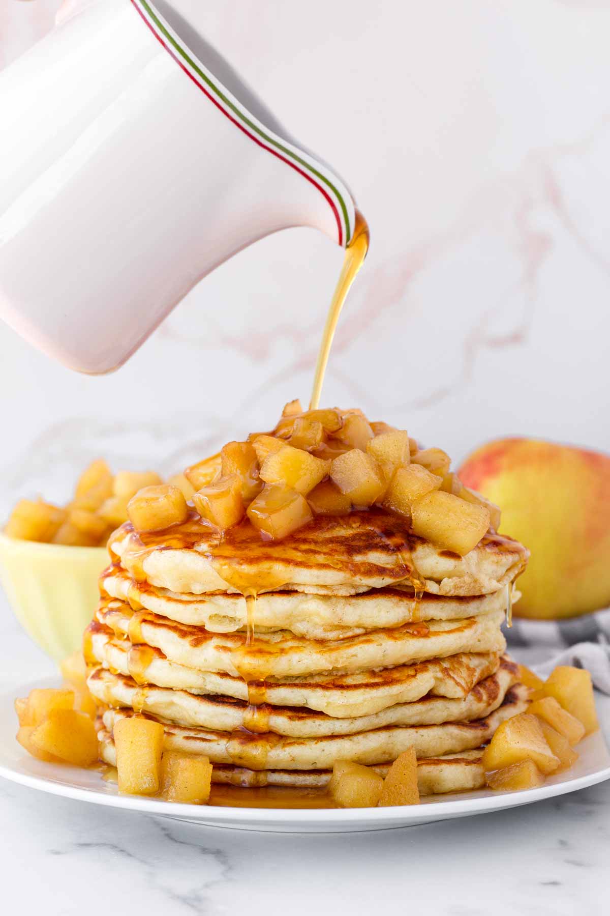 pouring maple syrup over pancakes with apple topping