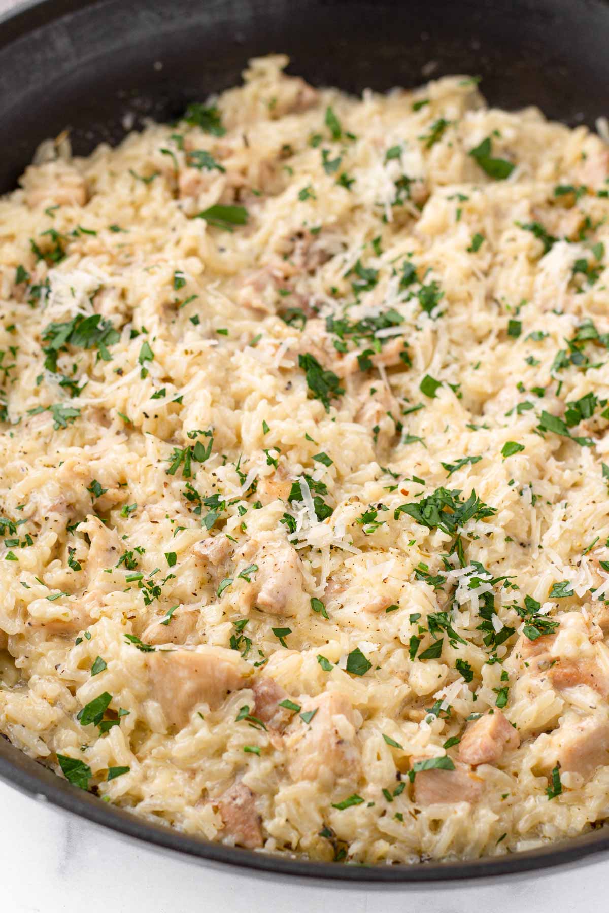 a skillet with creamy rice and chicken with parsley garnish