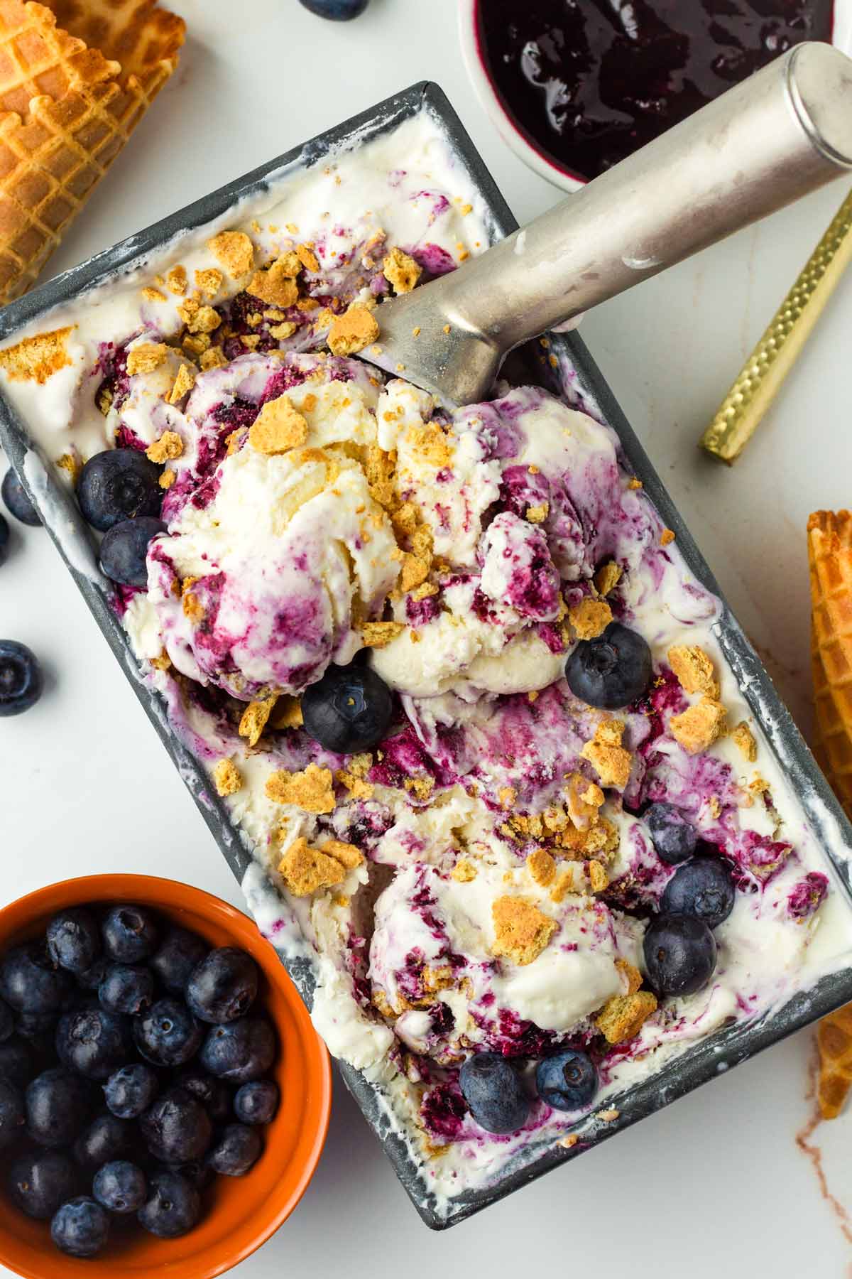 decorated blueberry cheesecake ice cream in a container and waffle cones around it