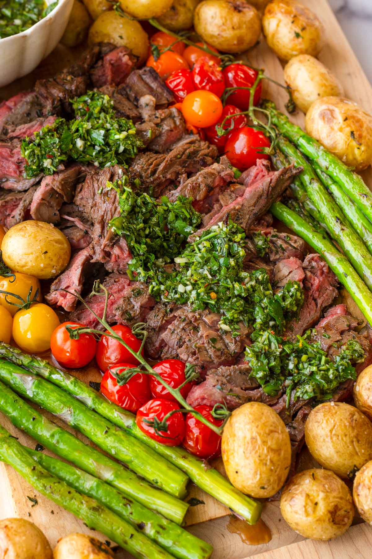 wooden platter with sliced skirt steak, chimichurri sauce, and grilled vegetables