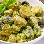 creamy pesto potato salad with garnish on bowl