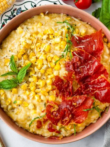 bowl of sweet yellow corn risotto with crispy prosciutto on top