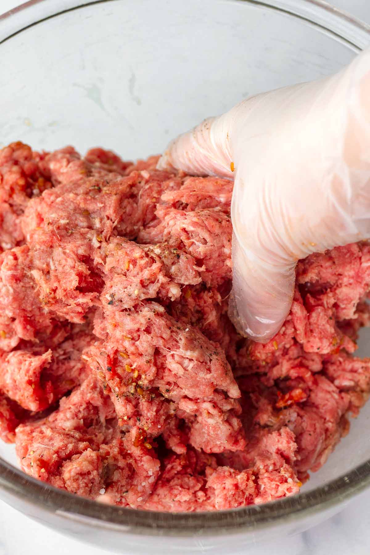 using hands to mix ground beef with seasoning in a bowl