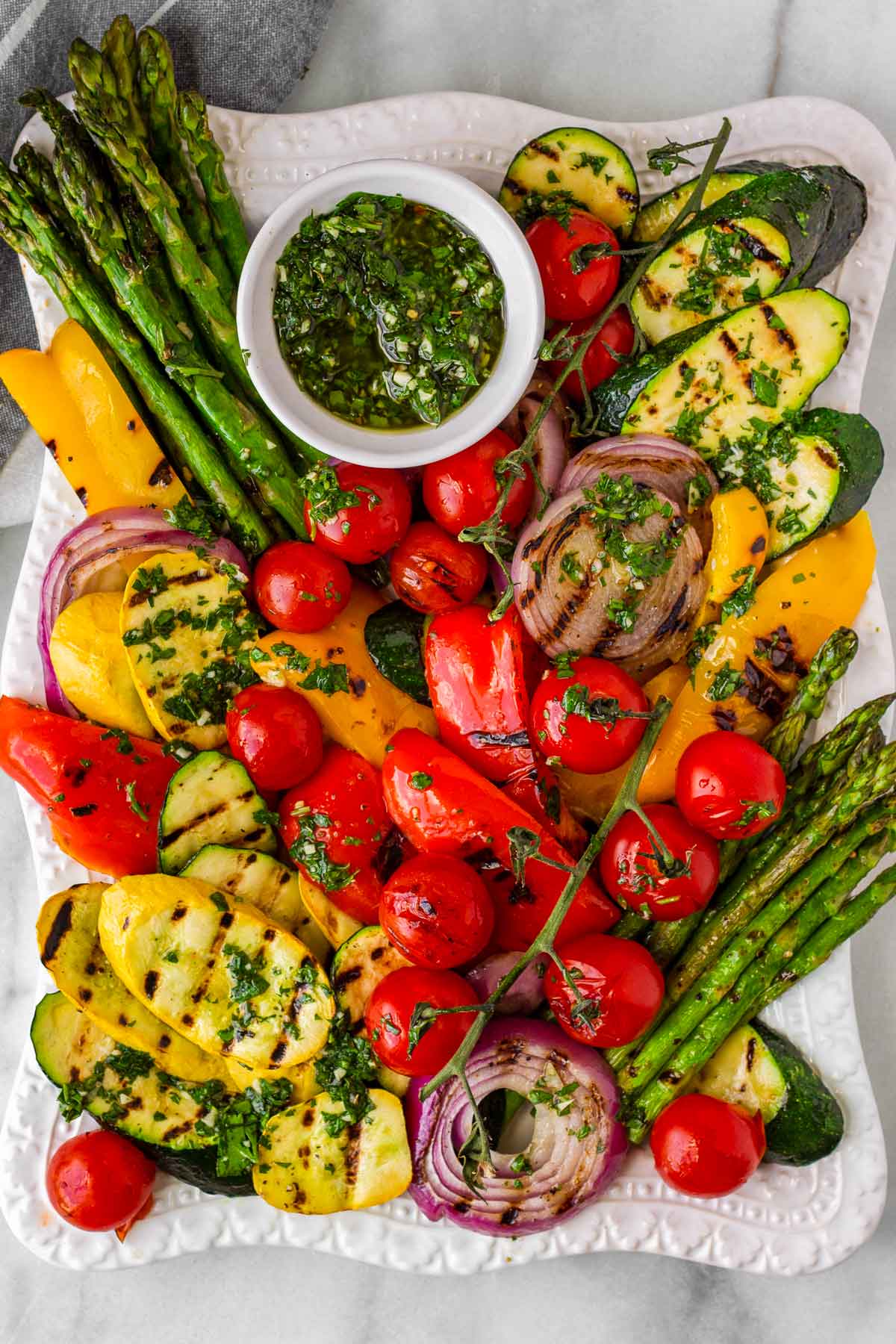 colorful grilled vegetables arranged on a rectangular platter with sauce