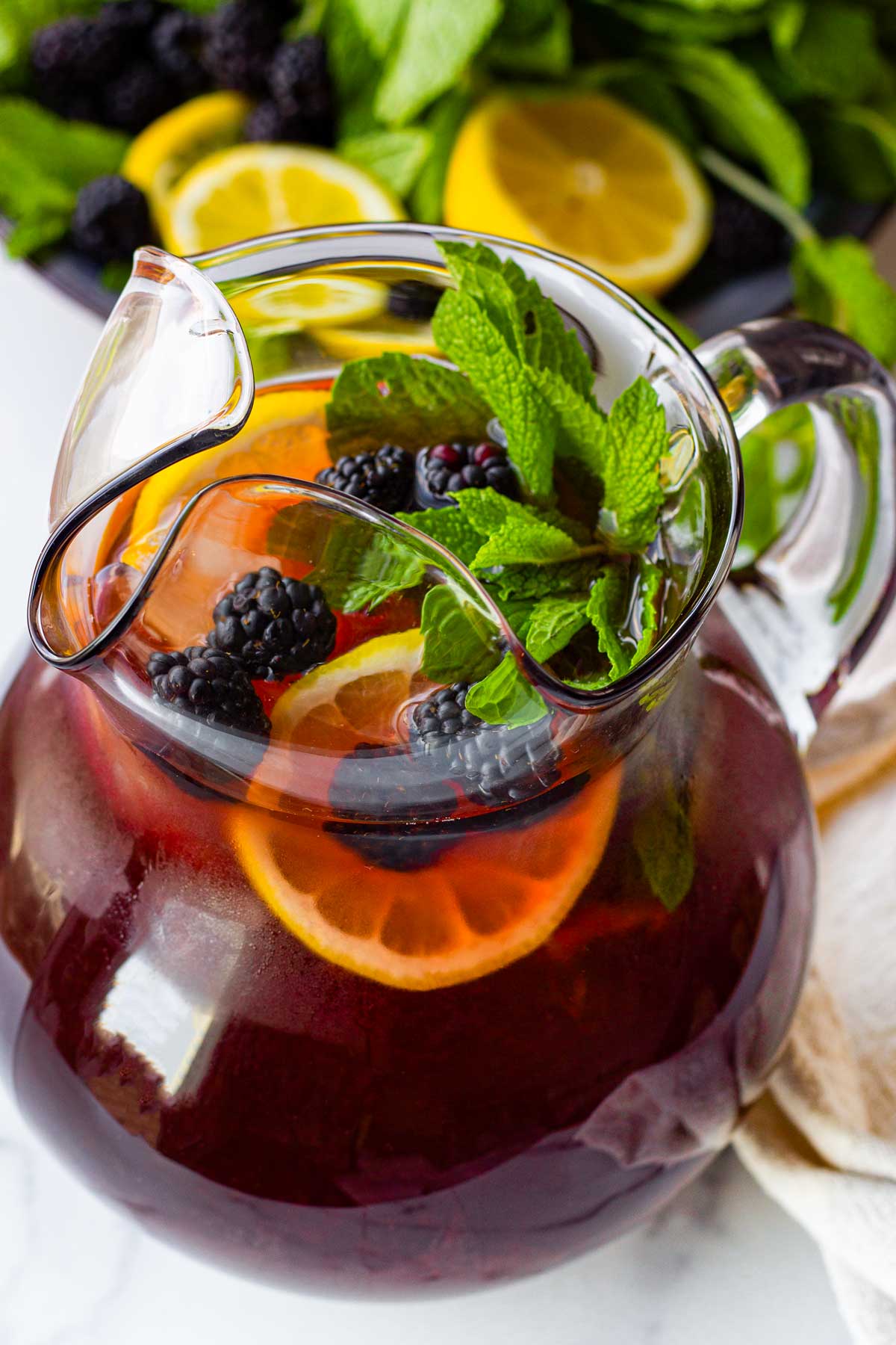 a pitcher of blackberry iced tea with lemon, blackberry, and mint garnish