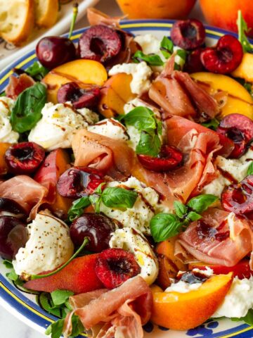 plate of fresh peach salad with burrata, cherries, and prosciutto served with baguette