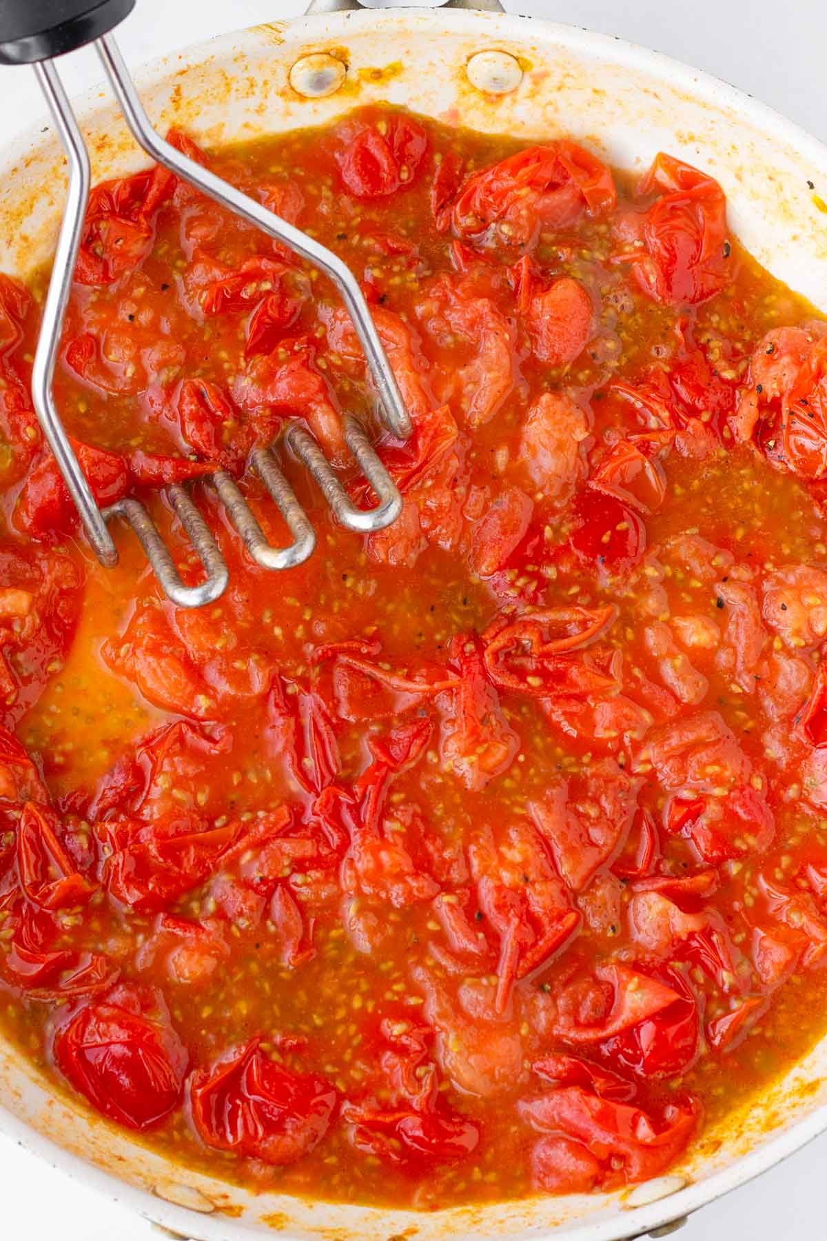 pressing cooked down cherry tomatoes with a masher
