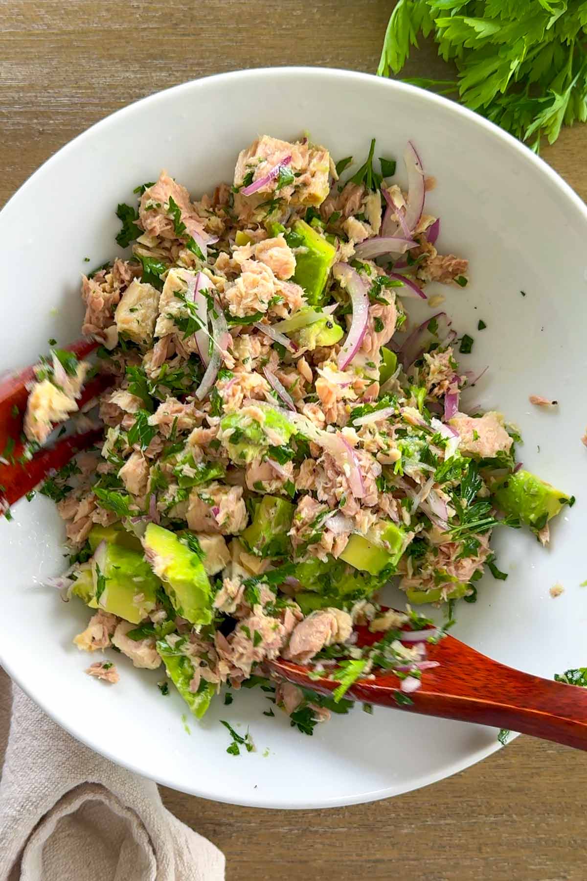 tossing avocado tuna salad with wooden serving spoons