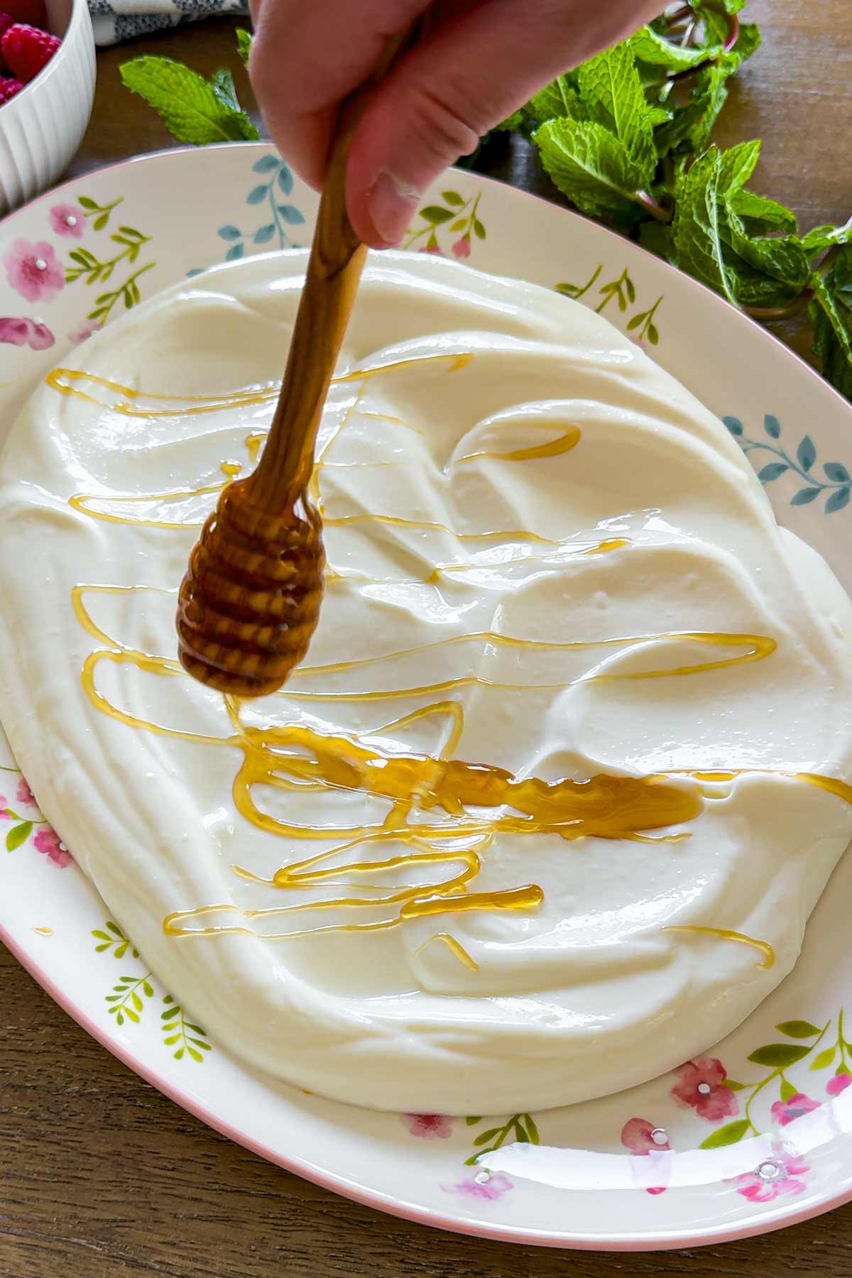 drizzling honey over a bed of yogurt on an oval plate