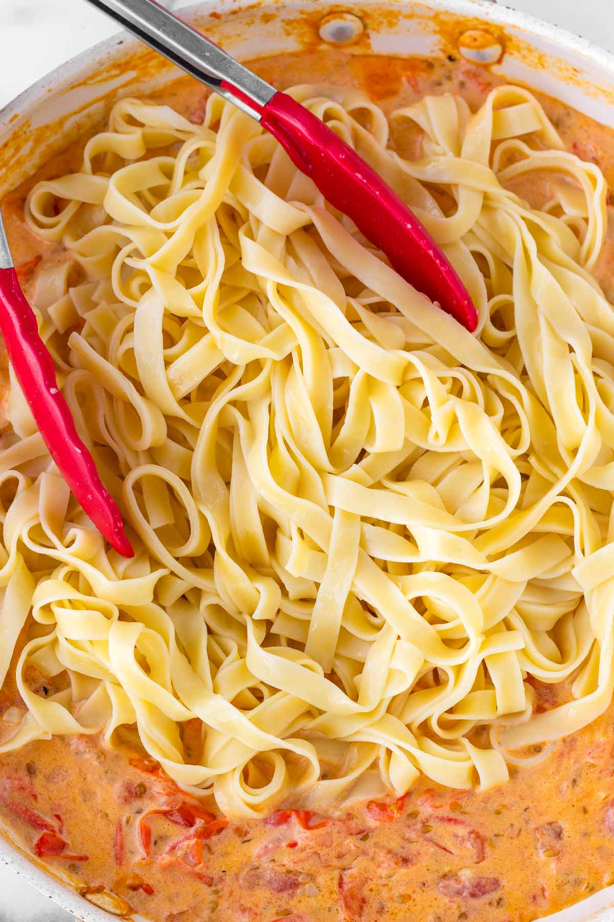 adding cooked pasta to the skillet with sauce
